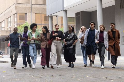 Multicultural young professionals walking in urban plaza, laughing and carrying coffee