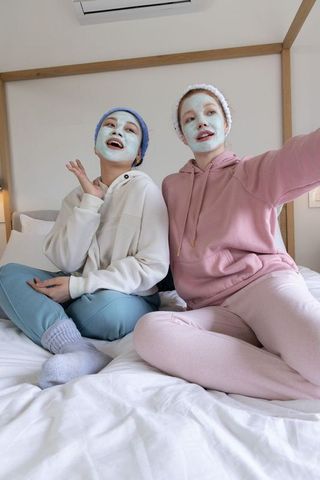 Friends wearing face masks in pastel loungewear enjoying at-home spa night and taking selfie