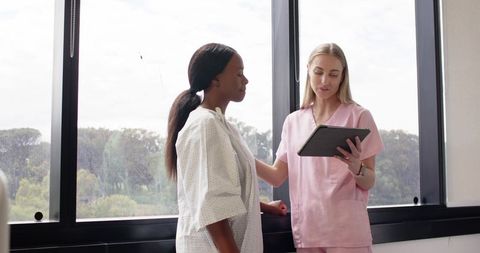 Clinician Consulting Black Patient Using Tablet in Bright Clinic with Window View