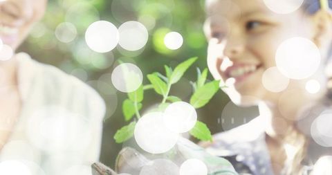Smiling girl holding green seedling with elder woman in sunlit garden bokeh