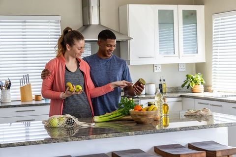 Couple reading jar label while preparing fresh fruits and vegetables in modern kitchen