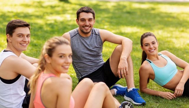 Smiling friends resting on grass after run, young adults enjoying outdoor fitness break