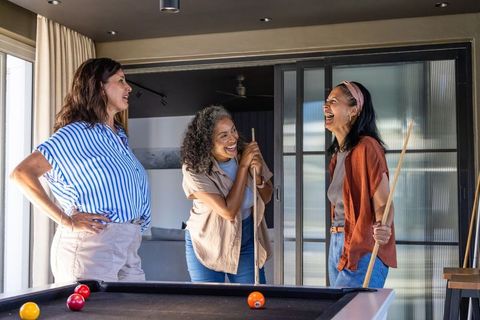 Diverse women laughing and playing pool in modern home rec room
