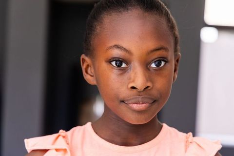 African girl gazing calmly in soft light interior portrait wearing pink ruffle top