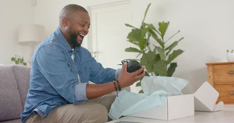 African american man unboxing wireless headphones at home, joyful reaction to new gadget