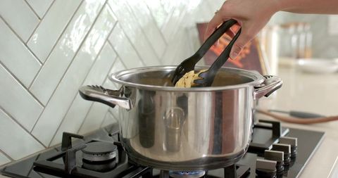 Home cook stirring ribbon pasta in stainless pot on gas stove with herringbone tile