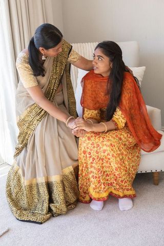 Mother supporting daughter in traditional indian attire at home