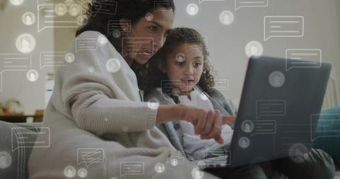 Mother pointing and guiding daughter on laptop, sharing cozy online learning moment