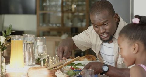 African American family sharing candlelit dinner as father serves roast chicken