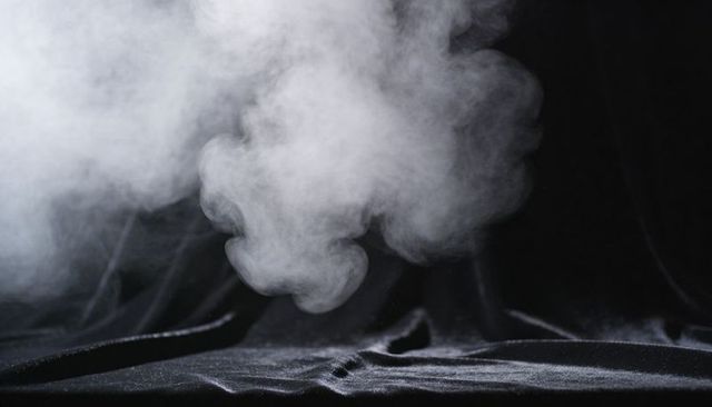 Billowing white smoke over black velvet fabric creating moody atmospheric texture and dust