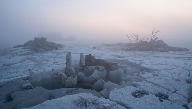 Frozen dawn: ice pillars and cracked slabs on misty arctic shore