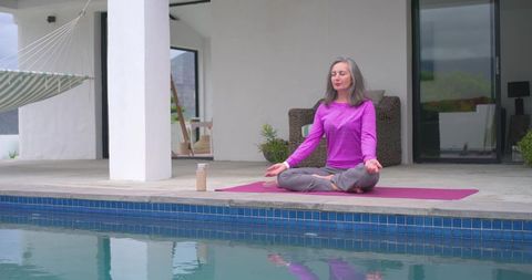 Mature woman meditating poolside on pink yoga mat practicing mindfulness and outdoor wellness