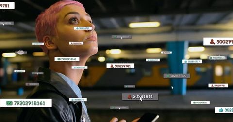 Woman holding smartphone with futuristic ids displays at train station