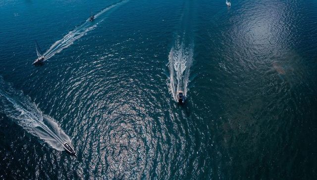 Aerial view of motorboat gliding across teal ocean leaving foamy wake and sun glare