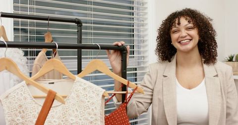 Smiling boutique stylist holding clothing rack with wooden hangers and dresses