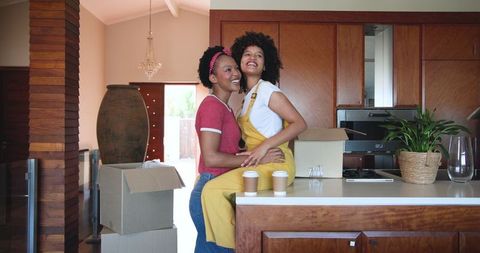 Cheerful Diverse Female Couple Embracing in New Home Kitchen
