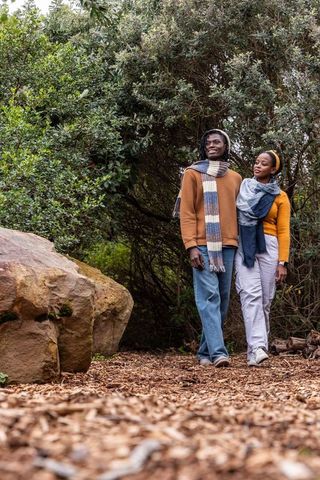 African american couple walking woodchip trail in forest wearing knit scarves and sweaters