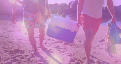 Two friends walking on sunlit beach carrying cooler and striped towel enjoying coastal day