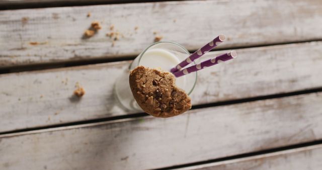 Appealing image perfect for use in food-related blogs, recipes, or social media. This charming stock photo showcases a glass of milk with a delicious cookie resting on the edge and two straws, creating a cozy and inviting atmosphere ideal for highlighting homemade desserts or snacks.