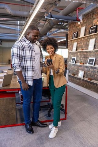 Diverse coworkers reviewing smartphone in modern office space