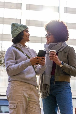 Diverse friends chatting with phone and coffee in urban plaza, casual winter attire