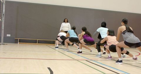 Female athletes team performing lunges in school gym during strength training with coach