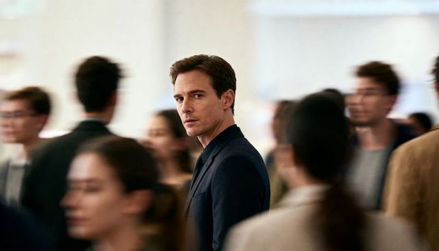 Focused businessman standing in busy modern concourse wearing dark suit and collared shirt