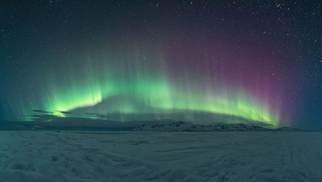 Aurora Borealis arching over snow-covered plain with distant mountains and starry sky