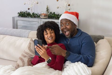 African american father and teen daughter sharing smartphone on cozy christmas couch