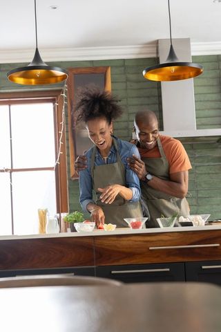 Couple cooking together at kitchen island embracing while preparing fresh ingredients