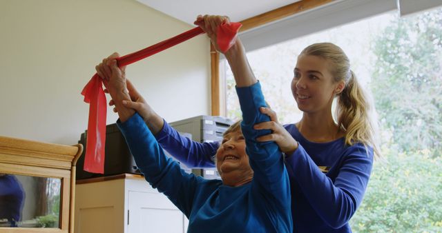 Female therapist guiding elderly woman in exercise with an elastic band indoors. Ideal for illustrations of healthcare support, senior rehabilitation, fitness programs for elderly, professional physiotherapy, and promoting active, healthy lifestyles for seniors.