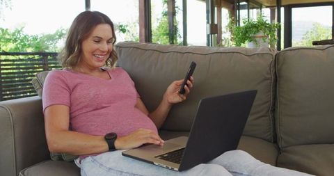 Pregnant Woman Relaxing with Laptop and Smartphone in Living Room