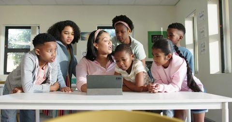 Teacher Guiding Diverse Students Around Tablet During Interactive Classroom Lesson