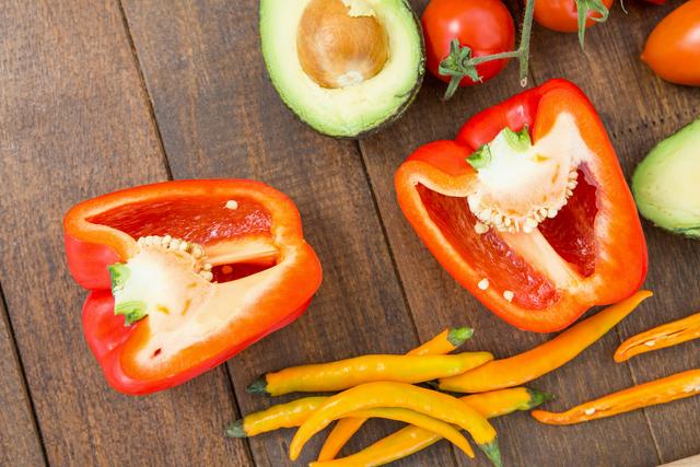 Close-up of various fresh vegetables including red bell pepper, avocado, chili peppers, and tomatoes on a wooden board. Ideal for use in cooking blogs, healthy eating promotions, organic food advertisements, and vegetarian or vegan recipe websites.