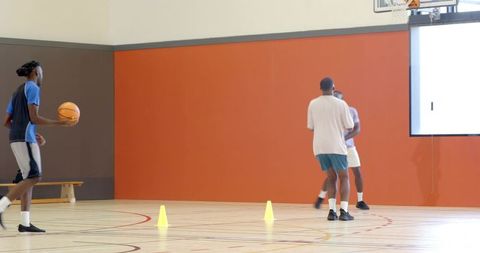 Basketball players practicing drill on hardwood court with cones and bright orange wall