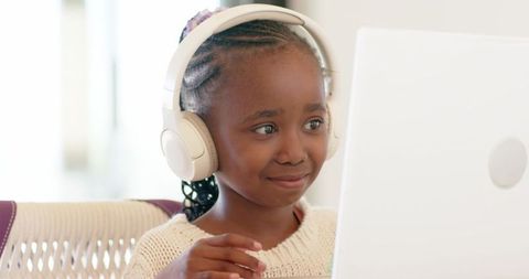 African American girl wearing headphones studying on laptop at home online learning