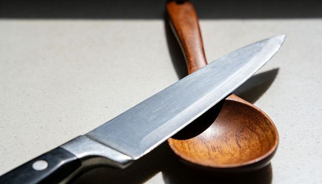 Chef knife and wooden spoon casting dramatic shadow on speckled countertop, close-up