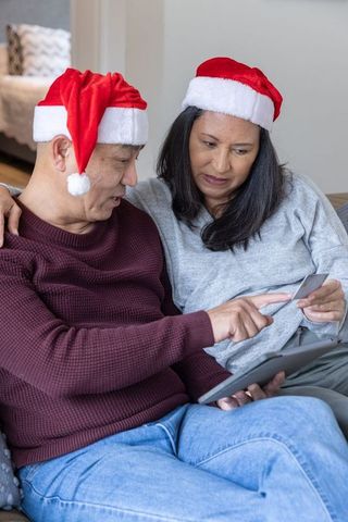 Senior Couple in Santa Hats Shopping Online with Tablet and Credit Card