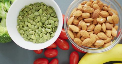 Healthy snack flatlay featuring pepitas and almonds with cherry tomatoes, banana, broccoli