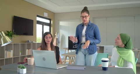 Diverse female team collaborating around laptop in modern office brainstorming meeting