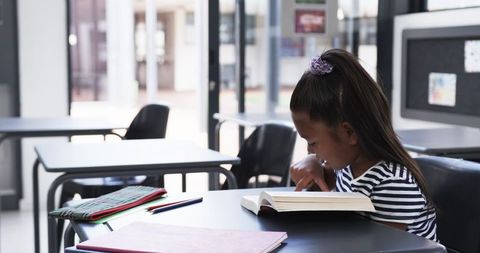 Young Girl Reading Book in Classroom with Concentrated Expression - Download Free Stock Images Pikwizard.com