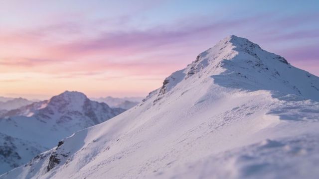 Snow-covered alpine ridge at sunrise with pastel sky and corniced summit