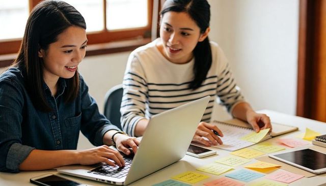 Two coworkers collaborating on laptop with sticky notes planning and brainstorming ideas