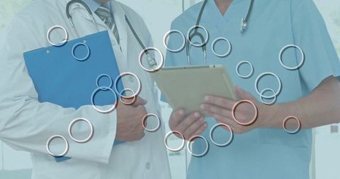 Doctors reviewing tablet together in hospital corridor with stethoscopes and clipboard