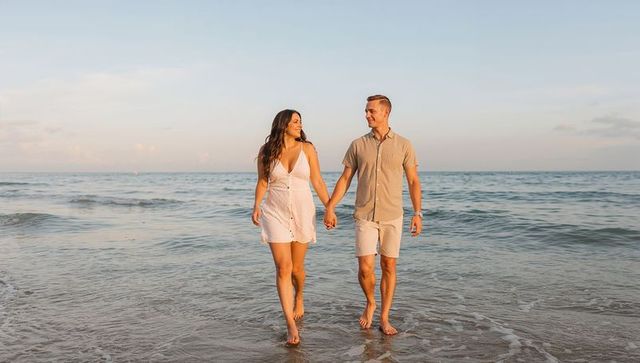 Romantic Couple Walking Hand-in-Hand on Sunlit Beach at Golden Hour, Barefoot, Vacation
