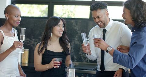 Friends toasting and laughing in modern kitchen during semi-formal cocktail gathering