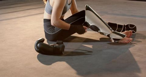 Female fighter adjusting shin guards while preparing for kickboxing training in gym ring