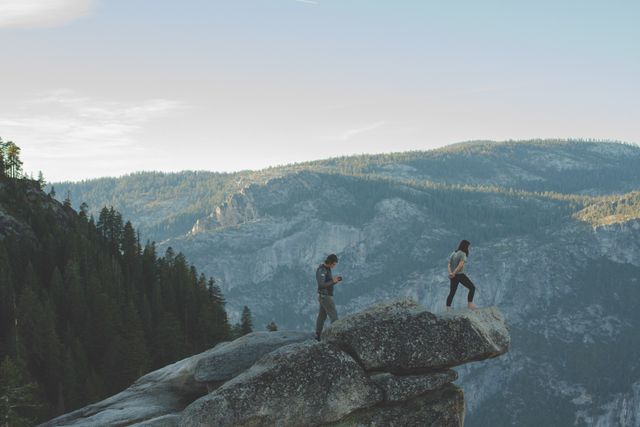 Two hikers exploring a rocky mountain ridge at sunset with scenic views of surrounding mountains and forests. Perfect for use in adventure travel blogs, nature exploration promotions, hiking guides, or outdoor lifestyle advertisements.