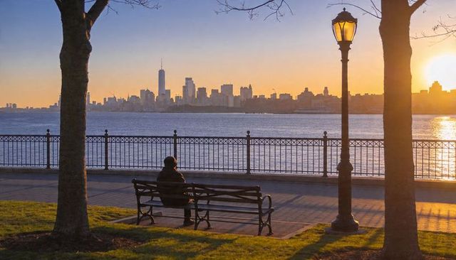 Solitary figure watching manhattan skyline at sunrise from riverside park bench