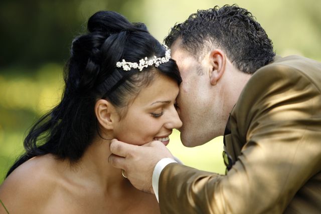 Groom is tenderly kissing bride's forehead, expressing love and affection. Ideal for use in wedding-related content, romantic event promotions, relationship advice articles, and Valentine's Day promotions.
